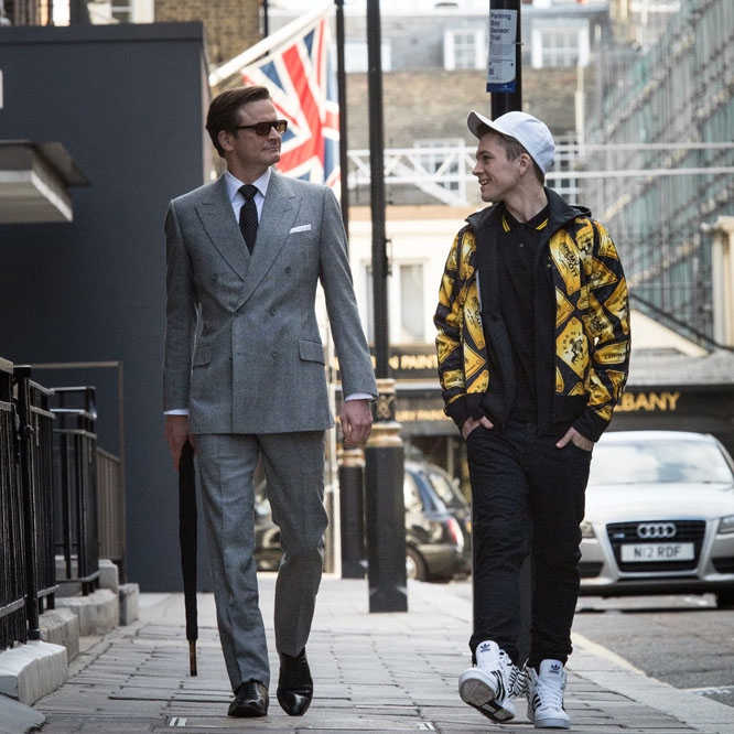 Eggsy and Harry from Kingsman walk down the street together, in their respective attire.