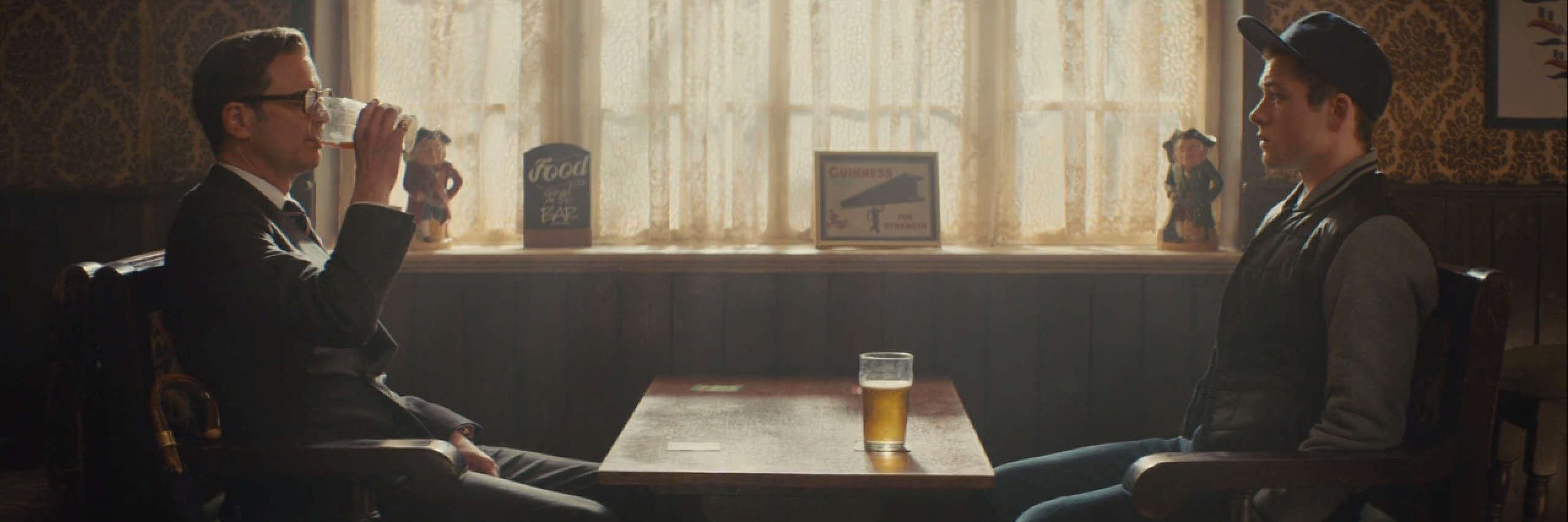 Eggsy and Harry from Kingsman sit in a pub, drinking beer.