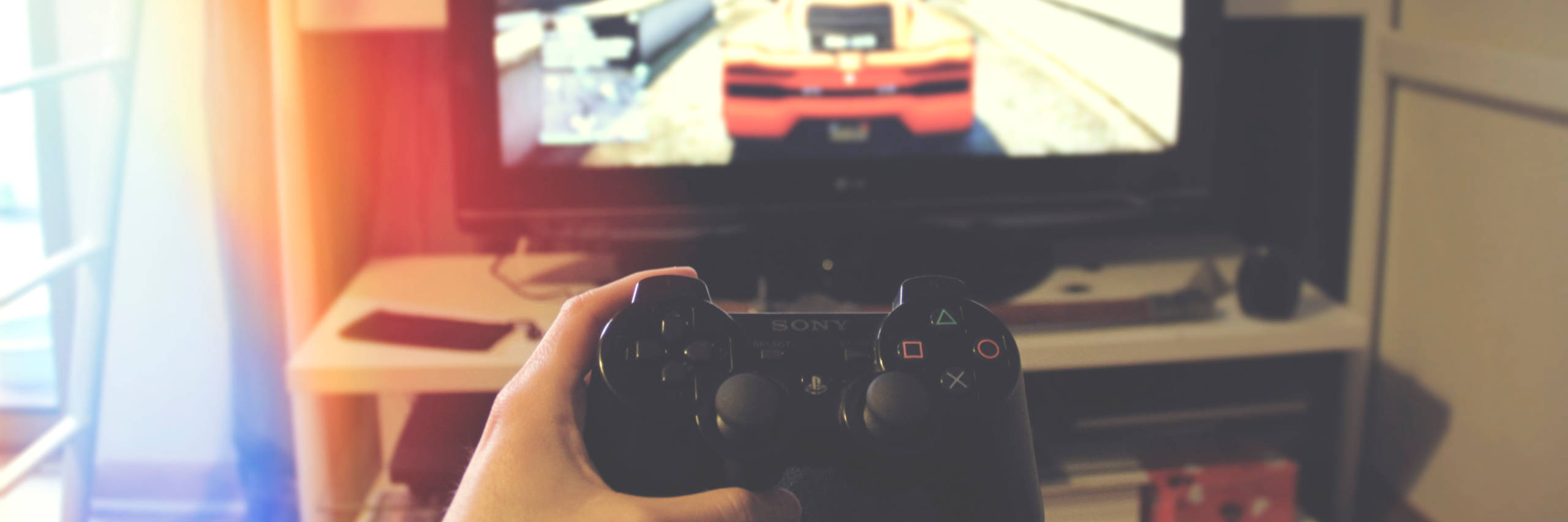 Hand holding a PS2 controller, with TV in the background.