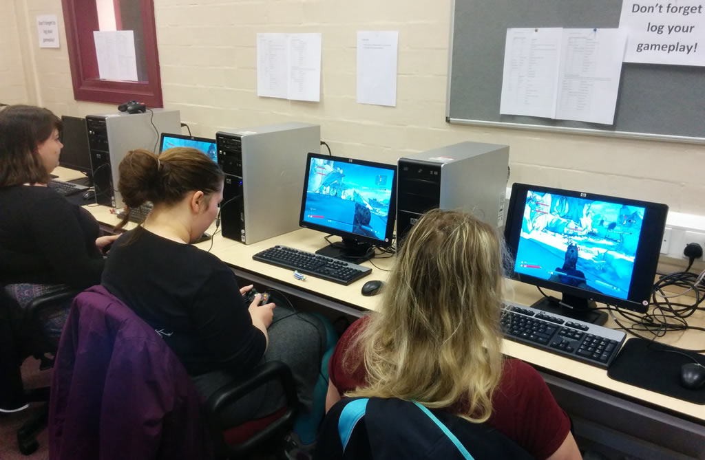 3 students sit at computers in a lab, playing video games.